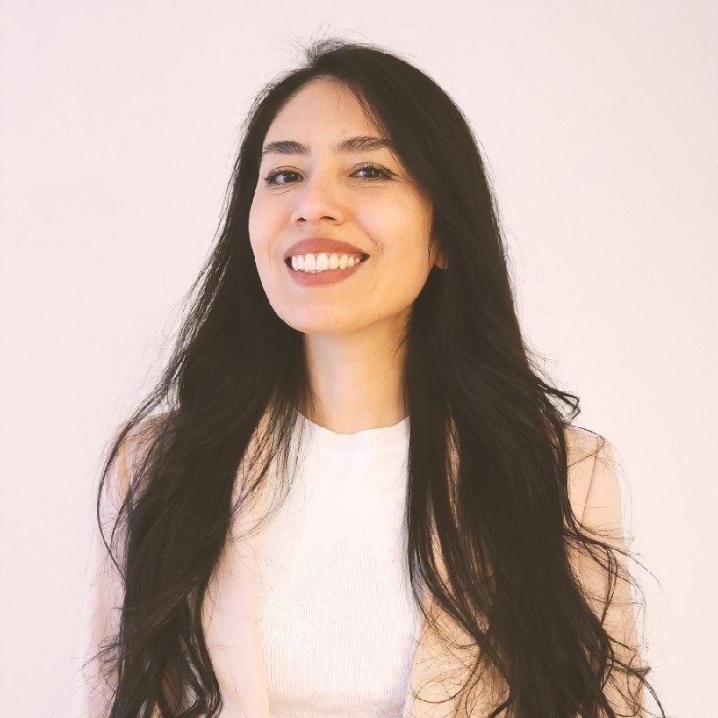 Young woman with dark long hair wearing a white shirt and a beige jacket